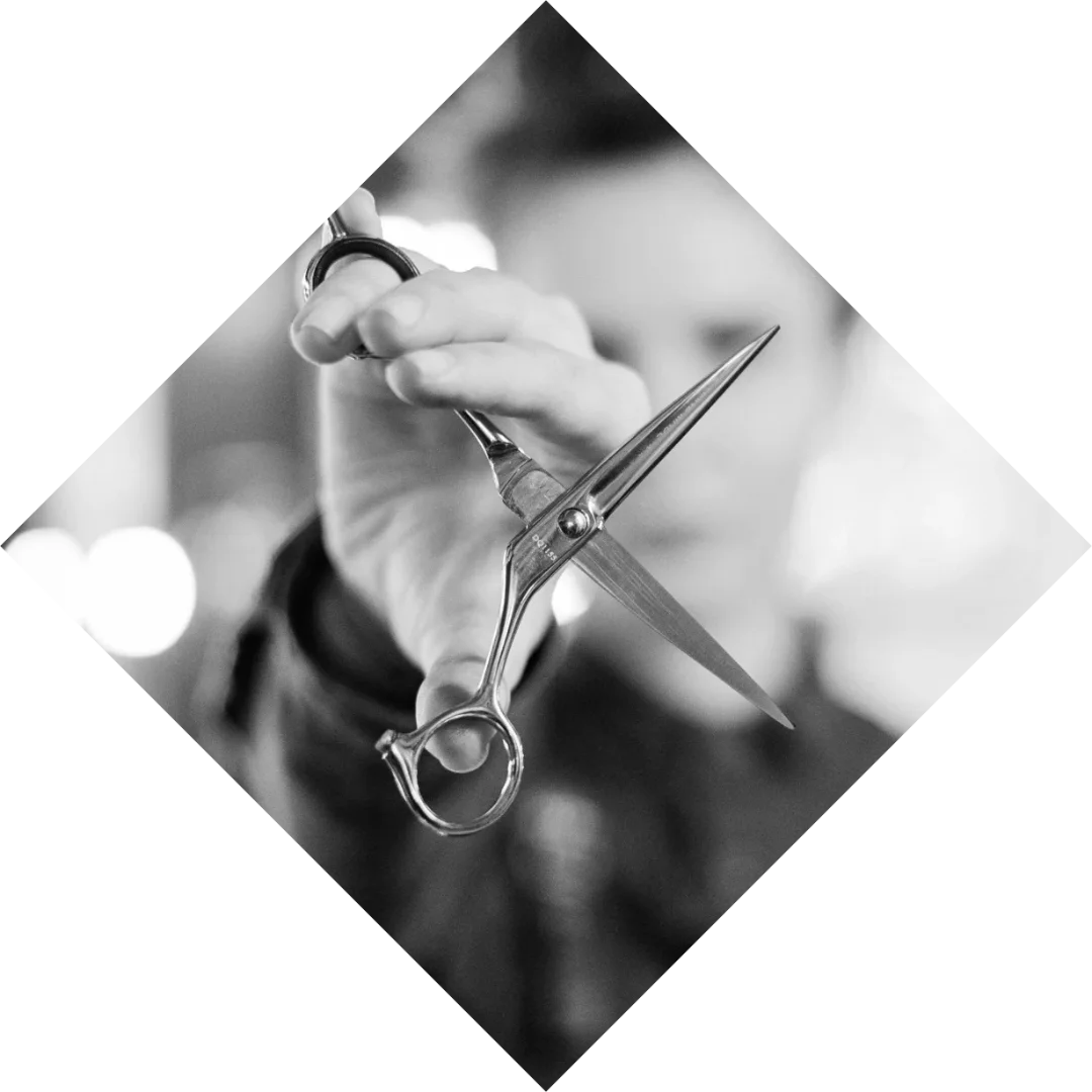 A person holding scissors sideways to show the blades and pivot point. Image cropped to be in the shape of a diamond.